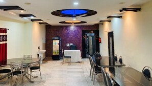 Un hall de hotel con mostrador de recepción, máquina expendedora y zona de comedor con mesas y sillas.