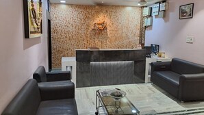 Un área de recepción con diseño moderno, que incluye una pared con estampado, un mostrador de recepción y dos sofás de cuero negro.
