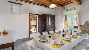A dining area with a long table set for a meal, white chairs, and a wooden ceiling. - Il Pratone 12 Emma Villas (Pomarance)