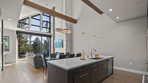 A modern kitchen with a large island, a dining area with a sofa and chairs, and a view of the outdoors through large windows. - 305A Boulder | 4BR/4BA Crystal Bay Lake View (Crystal Bay)
