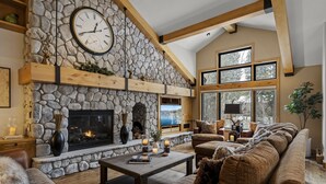 A cozy living room with a stone fireplace, leather sofa, and a large clock on the wall.