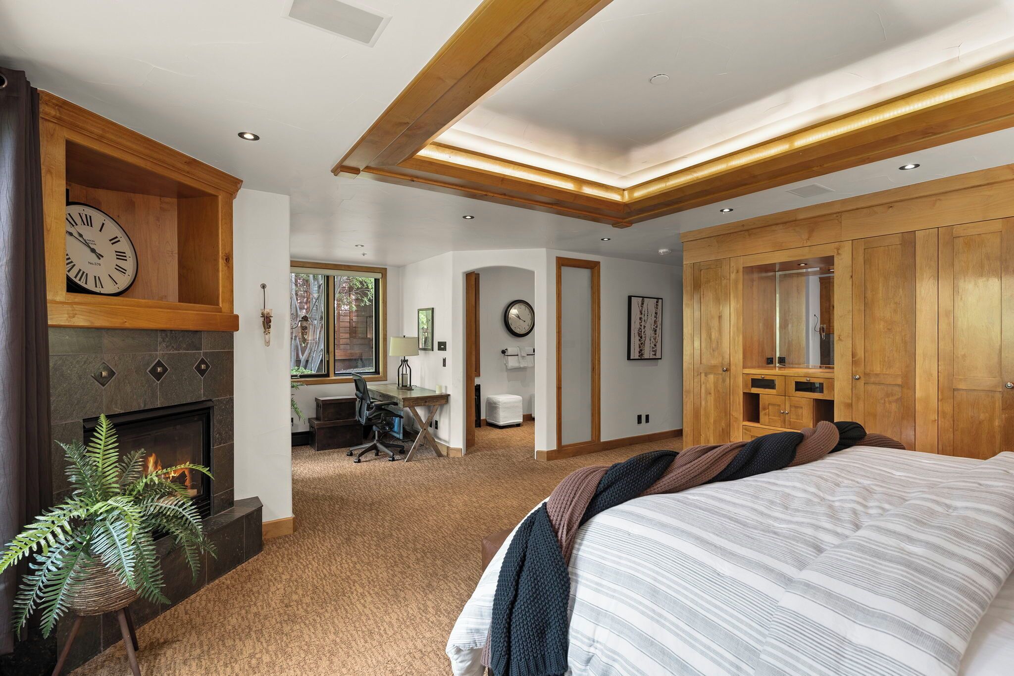 A spacious bedroom with a large bed, a fireplace, a desk, and a wardrobe.