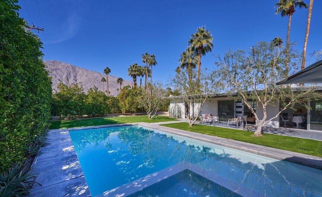 A swimming pool with a mountain backdrop, surrounded by palm trees and a well-maintained lawn.