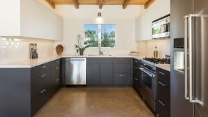 A modern kitchen with dark cabinets, stainless steel appliances, and a wooden ceiling. - Modern Olive 3  Mid Century Modern Retreat (Palm Springs)