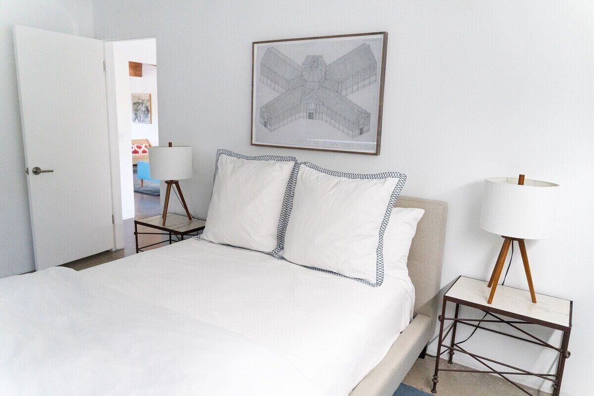 Een keurig opgemaakt slaapkamer met een bed, twee nachtkastjes, een lamp en een ingelijste architectuurtekening aan de muur.