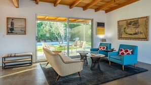 A modern living room with a wooden ceiling, large sliding glass doors to a patio, and a painting on the wall. - Modern Olive 3  Mid Century Modern Retreat (Palm Springs)