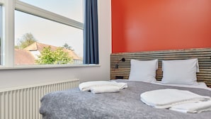 A hotel room with a bed, a window with a view of buildings, and a red wall. - Roskilde Danhostel (Roskilde)