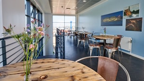 A modern dining area with wooden tables and metal chairs, large windows, and artwork on the walls. - Roskilde Danhostel (Roskilde)