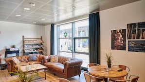 A cozy living area with a leather sofa, a wooden coffee table, and a round dining table with chairs. There is a bookshelf with books and a potted plant. - Roskilde Danhostel (Roskilde)