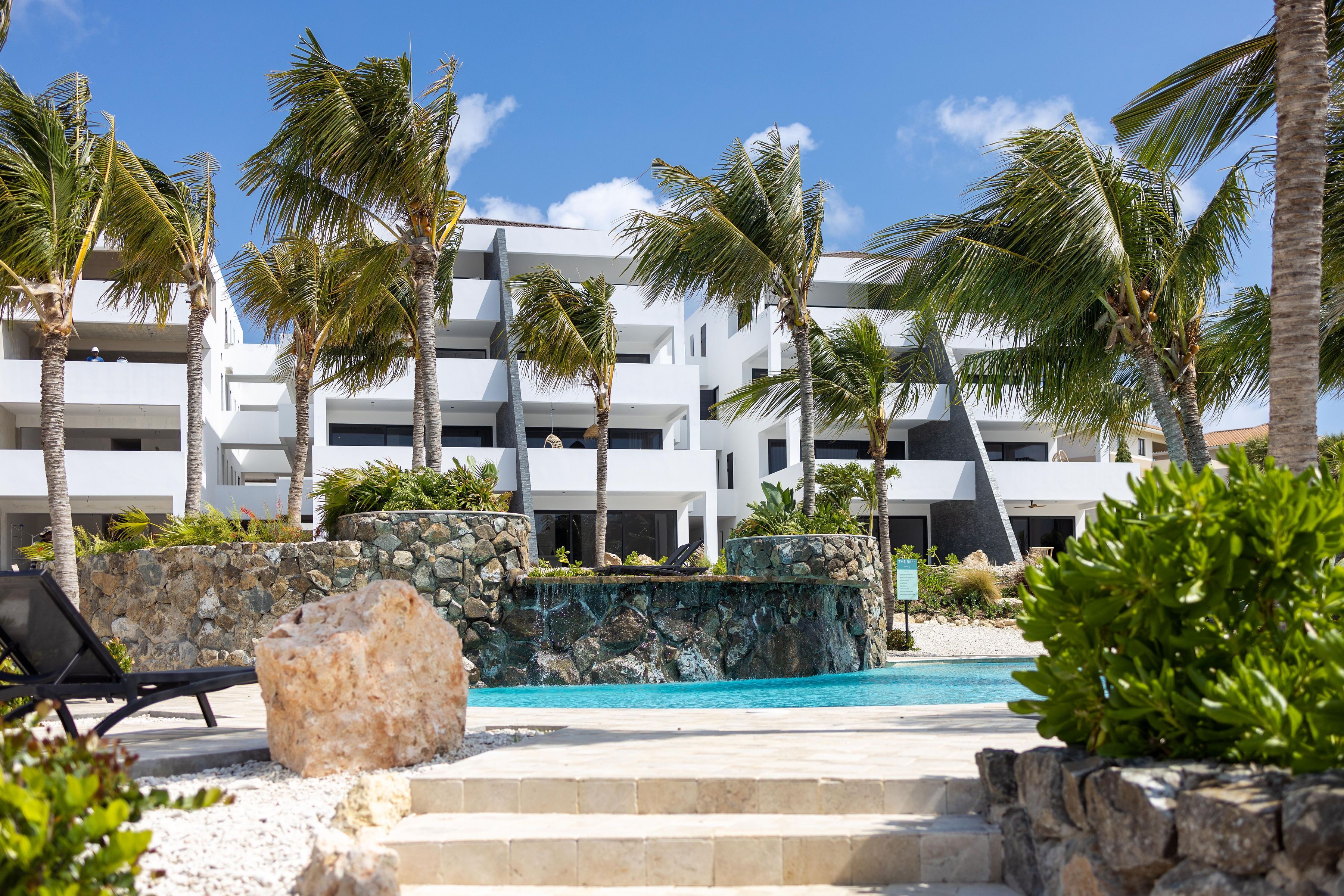 Un resort moderno con piscina, palmeras y un muro de piedra.