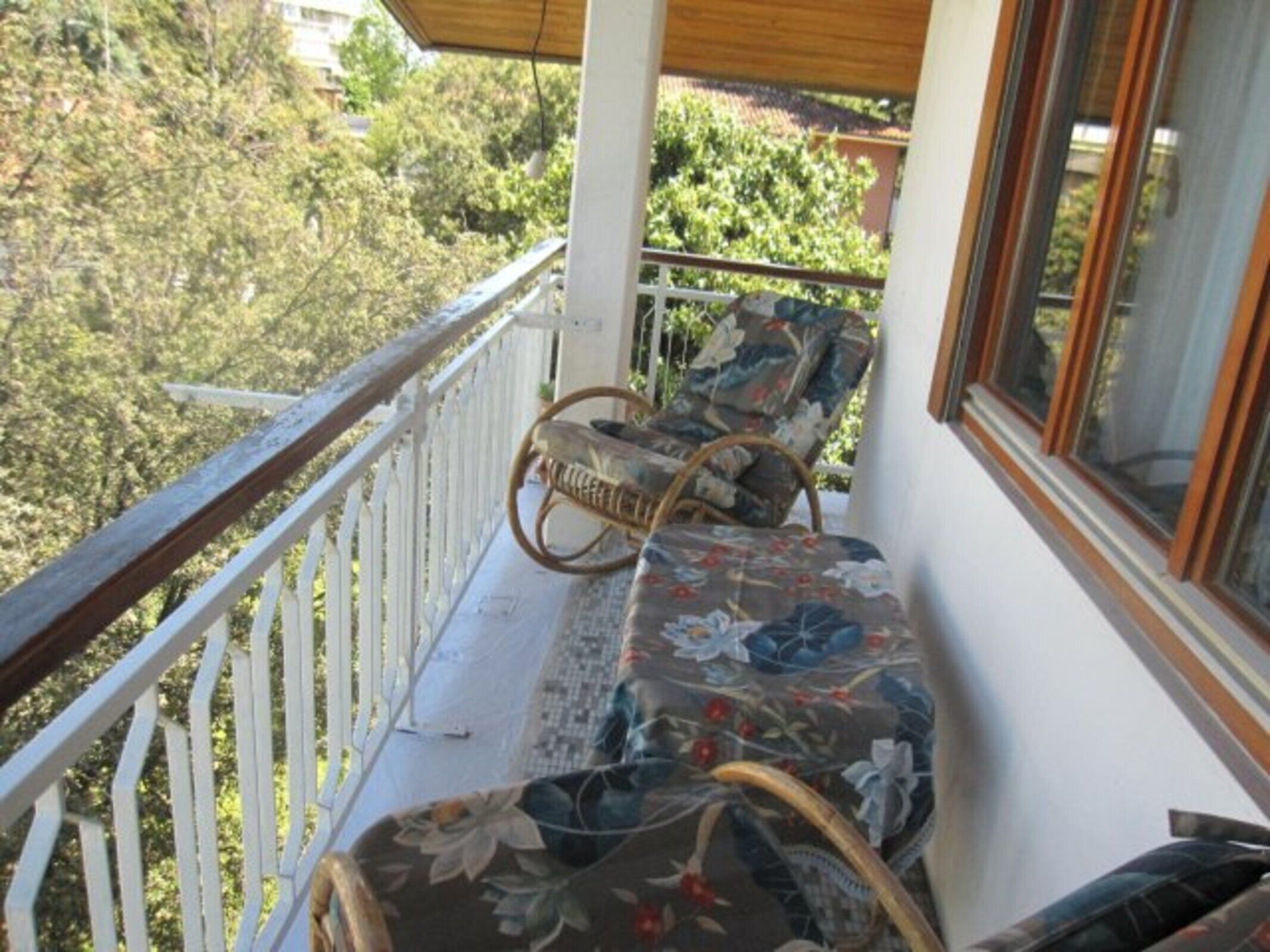 A balcony with wicker chairs and a sofa, overlooking a garden.