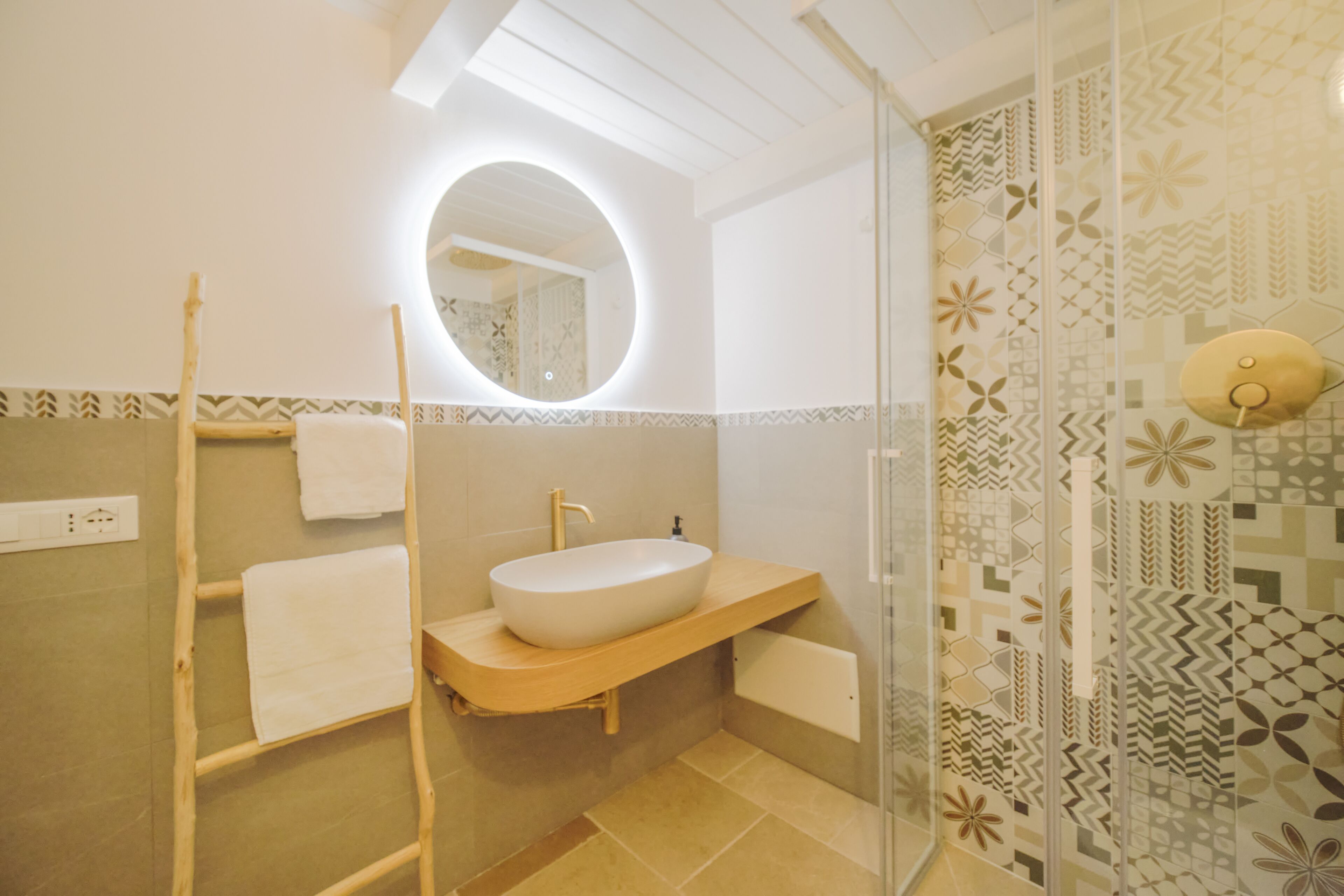 Un baño con tocador de madera, un espejo redondo y azulejos estampados.