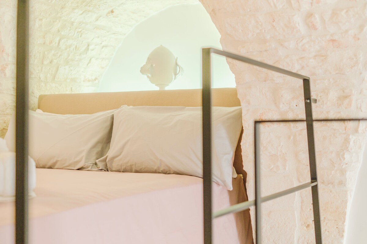 A bed with white linens in a room with a stone wall and a window.