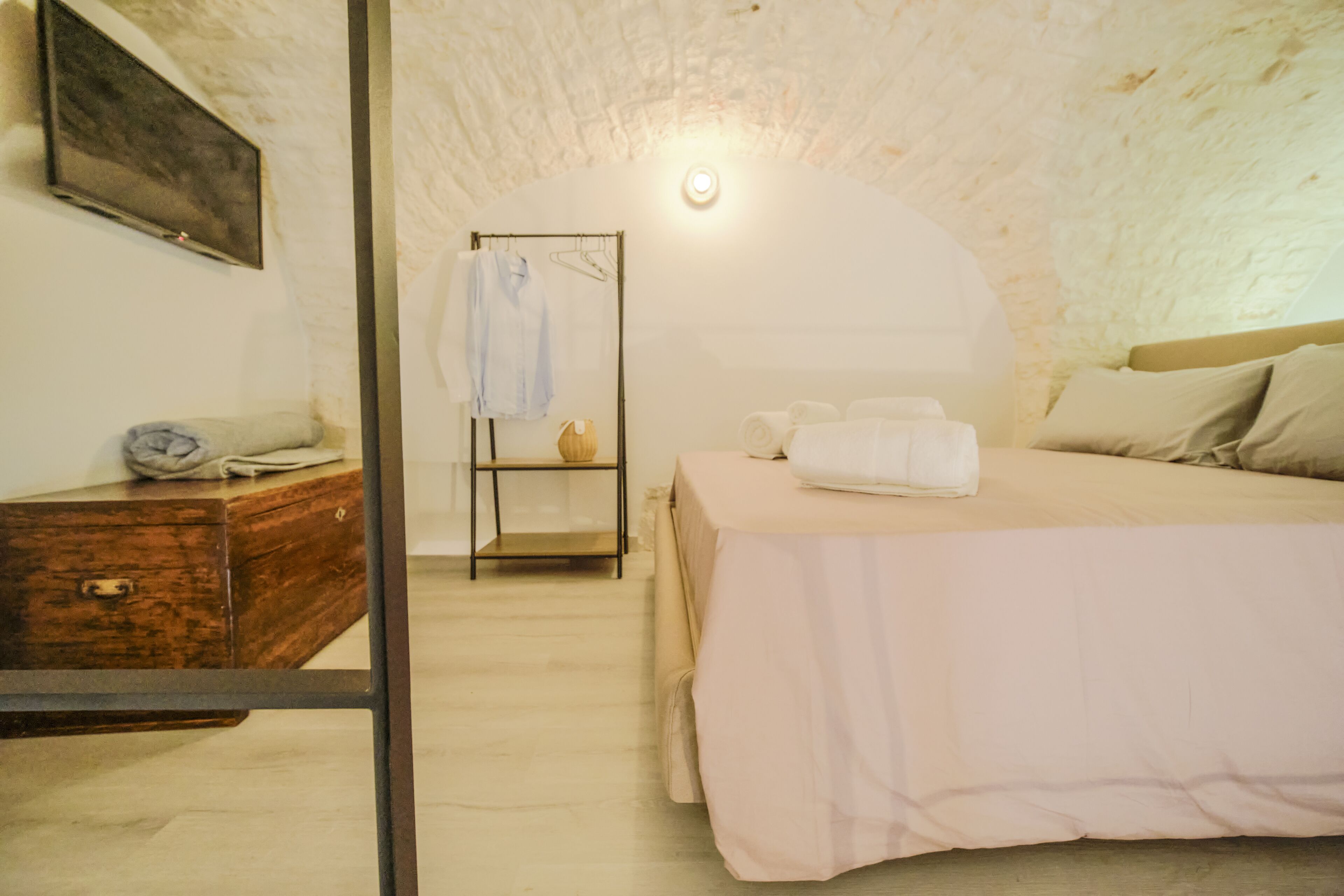 Une chambre à coucher comprenant un lit, une commode en bois, un portant à vêtements et un téléviseur fixé au mur.