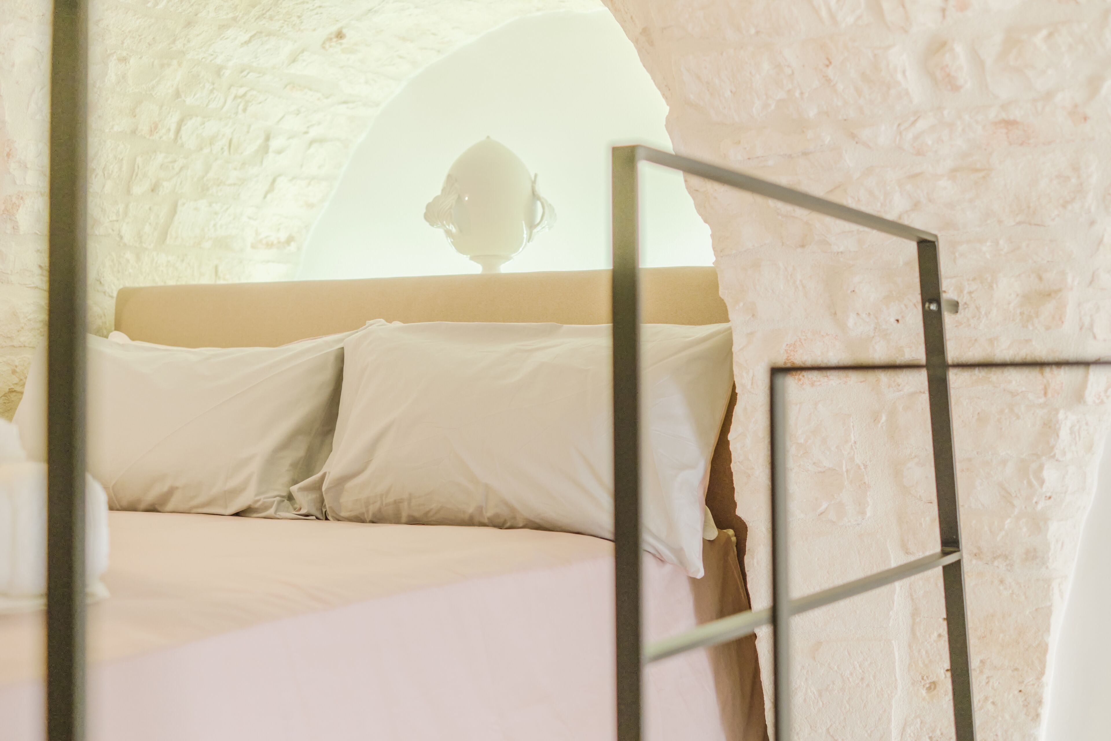 A bed with white linens in a room with a stone wall and a window.