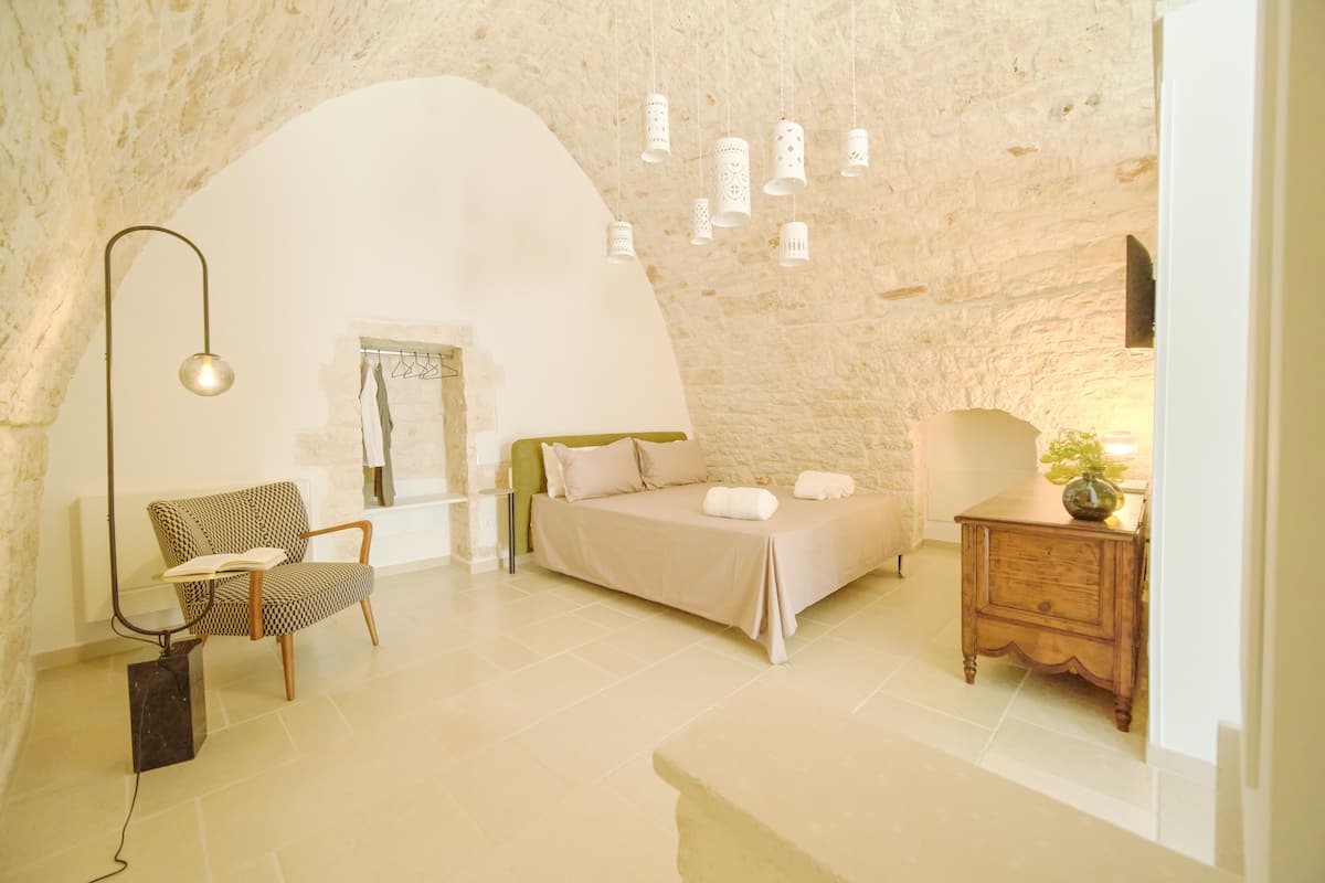 A bedroom with a bed, a chair, a nightstand, and a lamp.