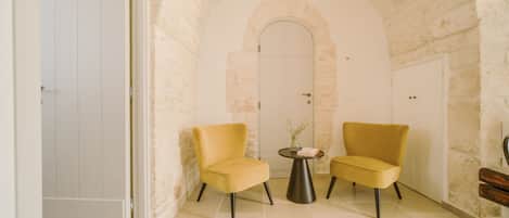 A room with a stone archway, two yellow chairs, a small round table with a vase, and a white door.