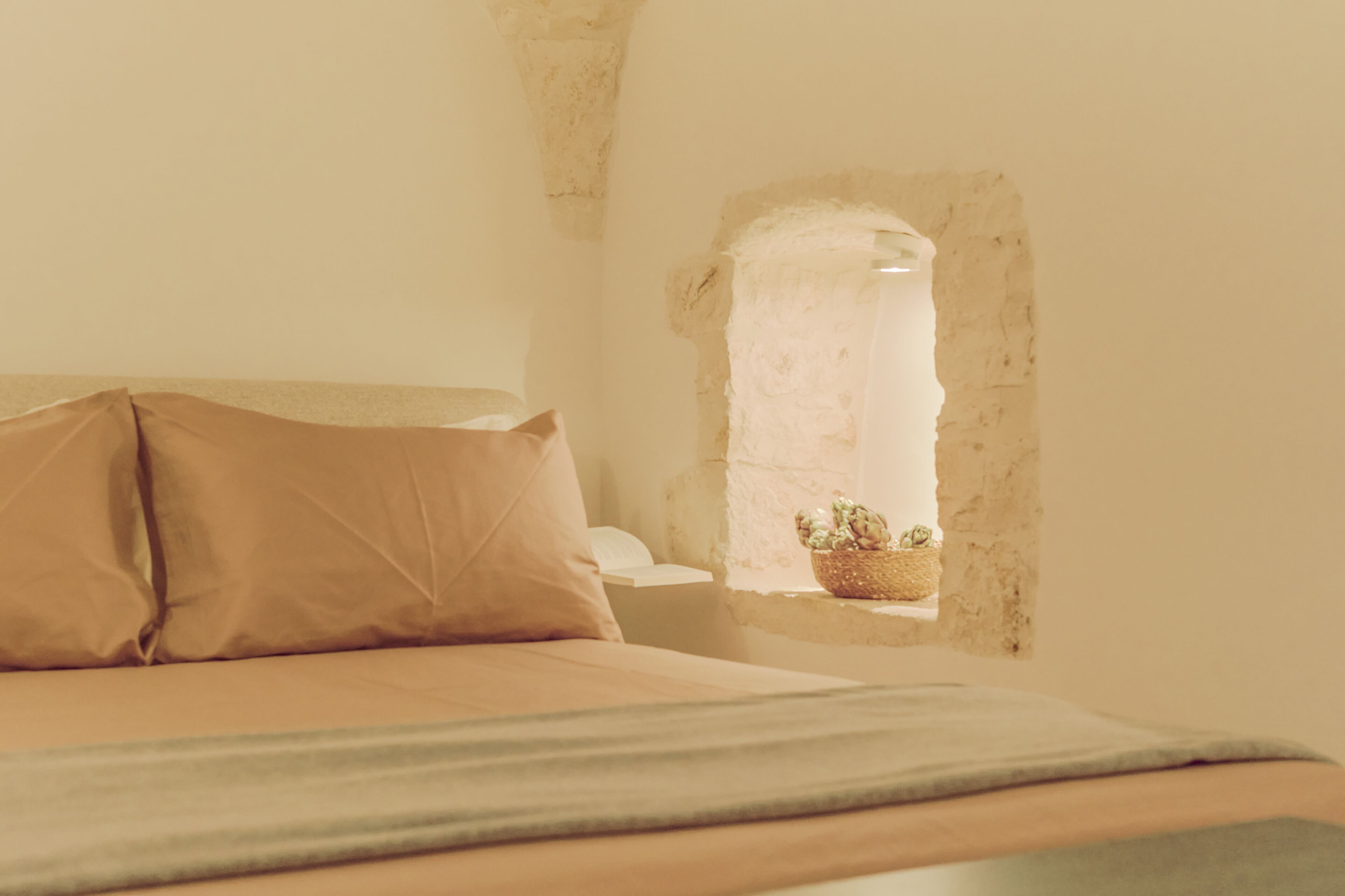 Un dormitorio con cama, almohadas, mesita de noche y ventana con vistas al exterior.