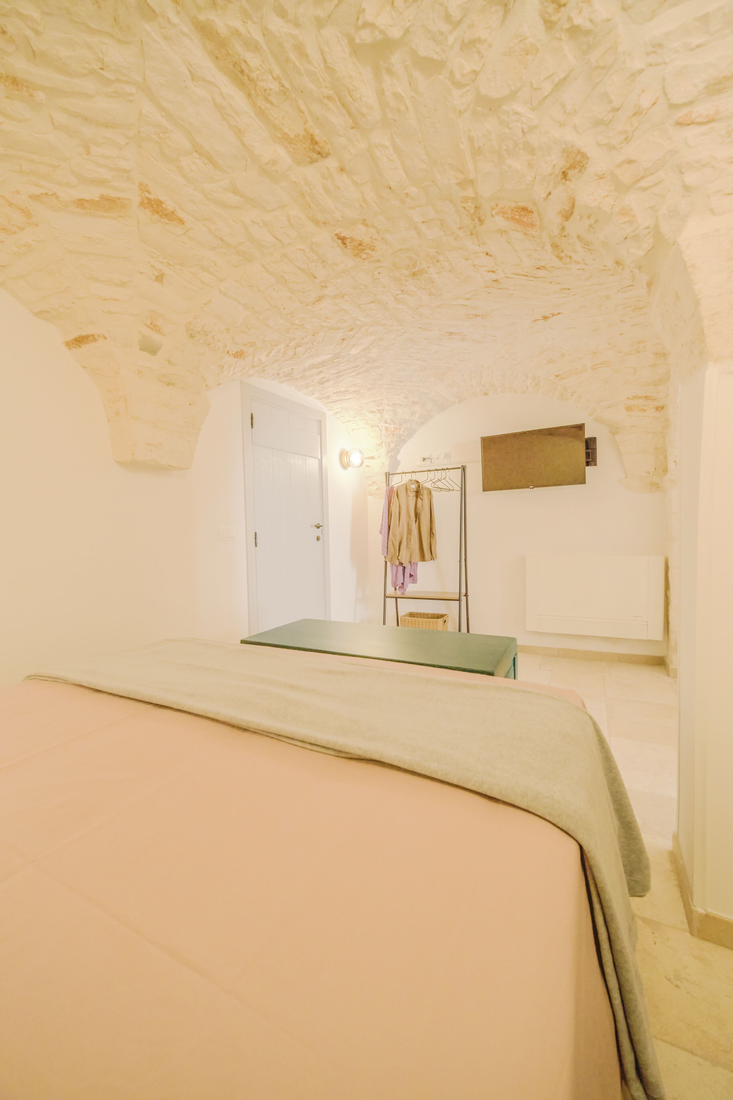 A room with a bed, a coat rack, and a door leading to another room.