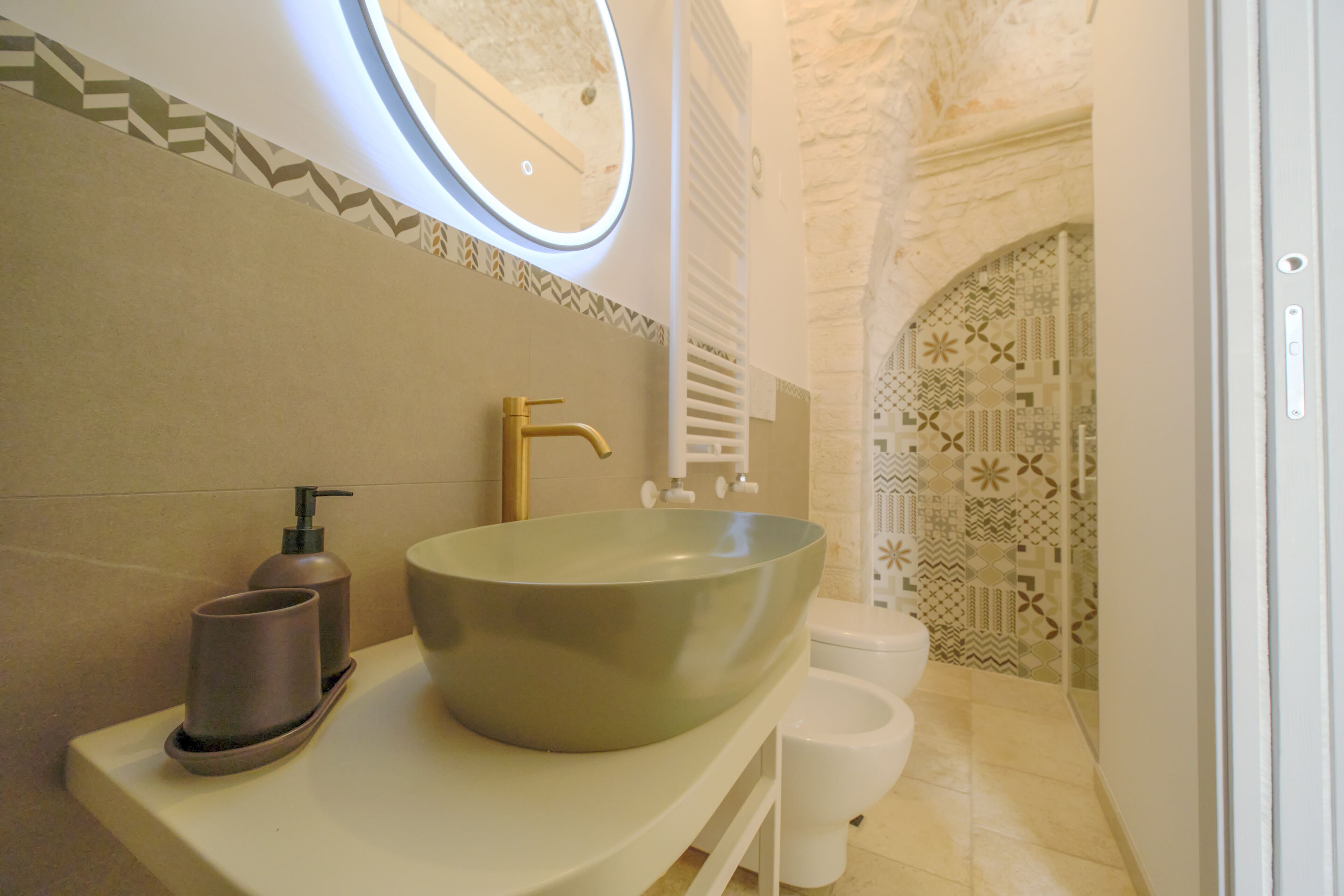Un baño con un lavamanos de pedestal, un grifo dorado, un espejo y baldosas con diseño.