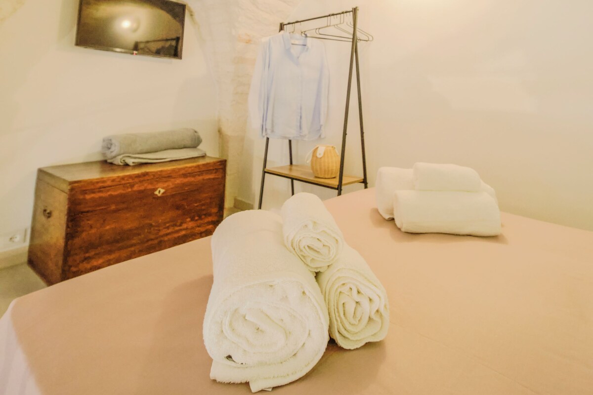 Una habitación acogedora con cama, cómoda de madera, toallero en la pared y un cuadro.