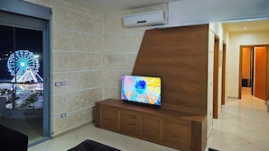 A modern living room with a TV on a wooden cabinet, a glass door leading outside, and an air conditioning unit on the wall. - Holiday 2-bed Apartment Seaview (Vlorë)