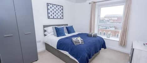 A bedroom with a bed, grey wardrobe, and a window with curtains.