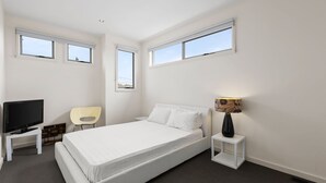 A modern hotel room with a large bed, a TV, a chair, and a lamp.