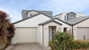 A modern two-story house with a garage, a small porch, and a well-maintained garden with tropical plants.