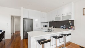 A modern kitchen with white cabinets, stainless steel appliances, a central island with bar stools, and a dark backsplash.