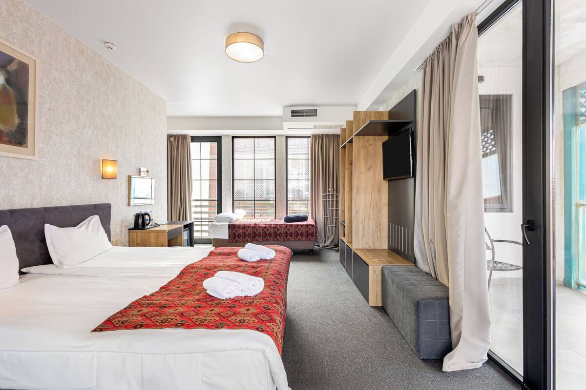 A hotel room with two beds, a desk, a TV, and a sliding glass door to the outside.