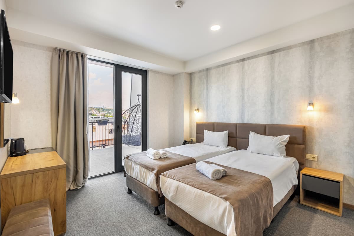 A hotel room with two beds, a desk, a chair, a TV, and a view of the city.