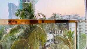 Vista desde una ventana con baranda de metal, que da a una zona residencial con varios edificios y palmeras.