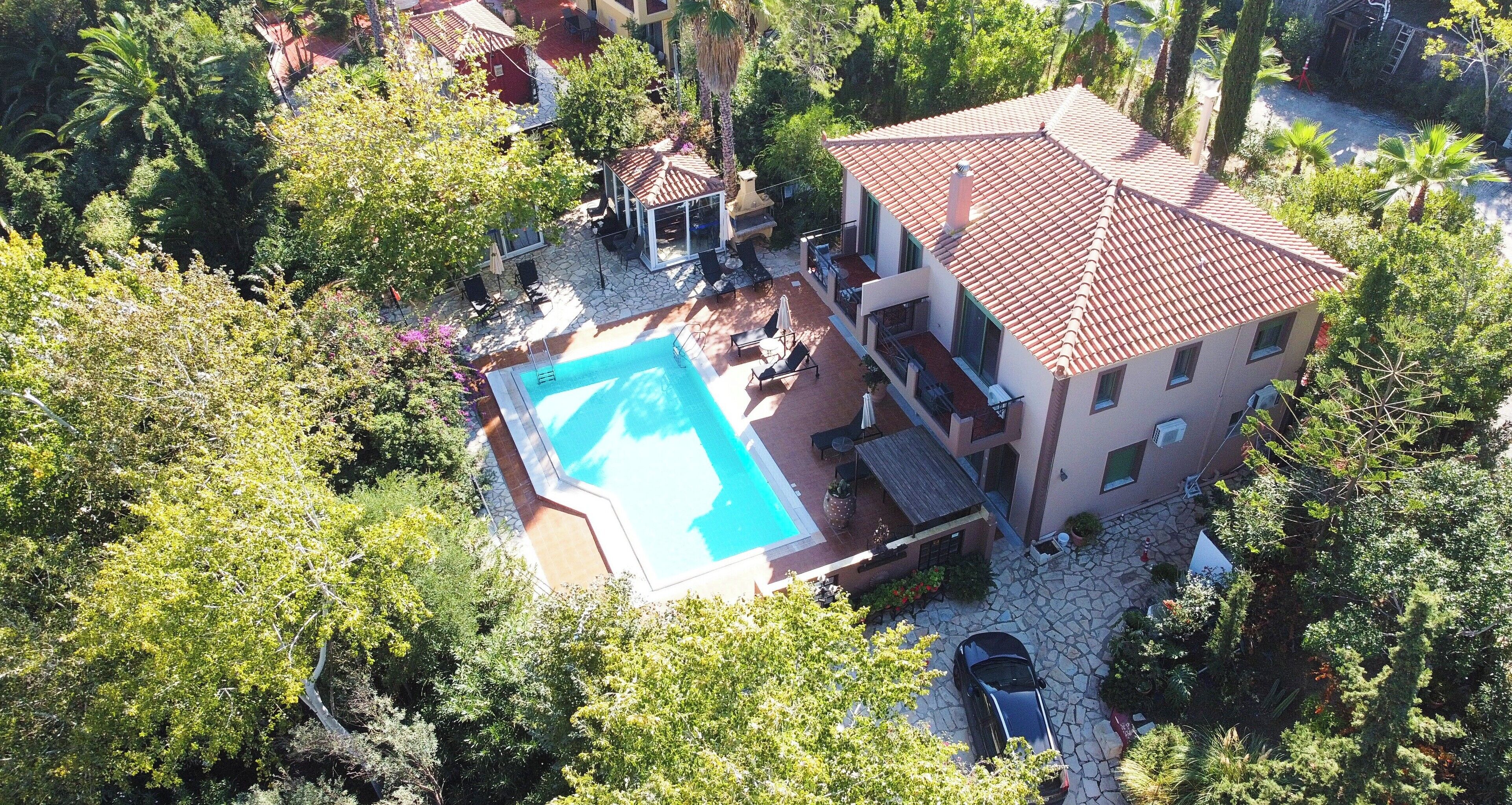 Una casa de dos pisos con piscina, rodeada de árboles y un patio de piedra.