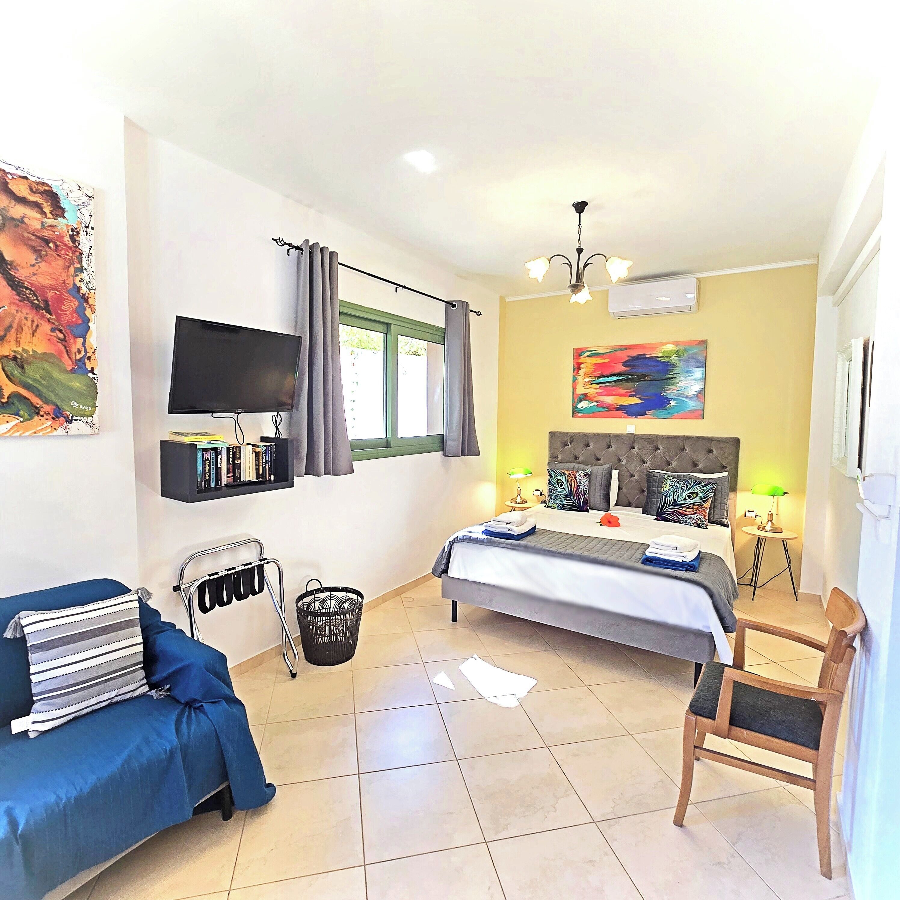 Un dormitorio con cama, televisión, estantería, silla y un cuadro.
