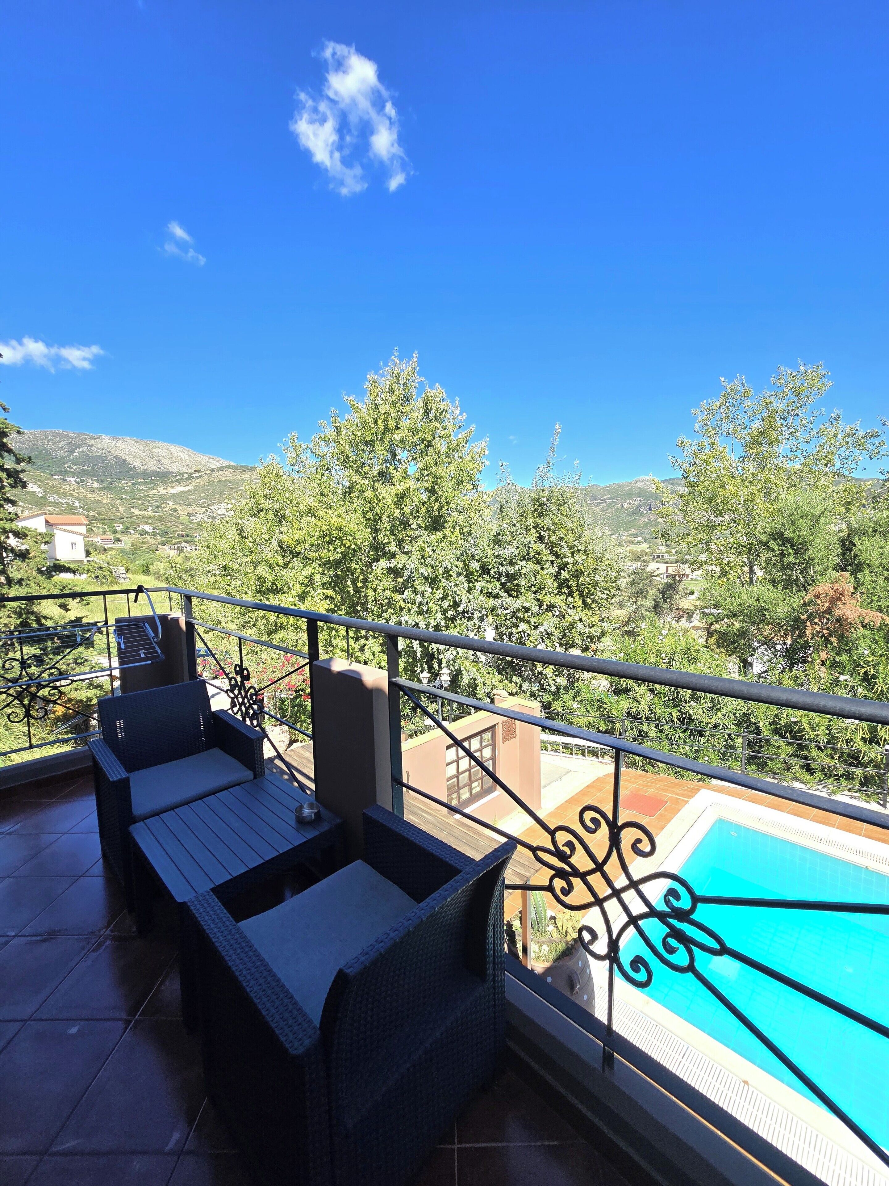 Uma varanda com mobiliário de vime, piscina e vista para uma paisagem montanhosa.