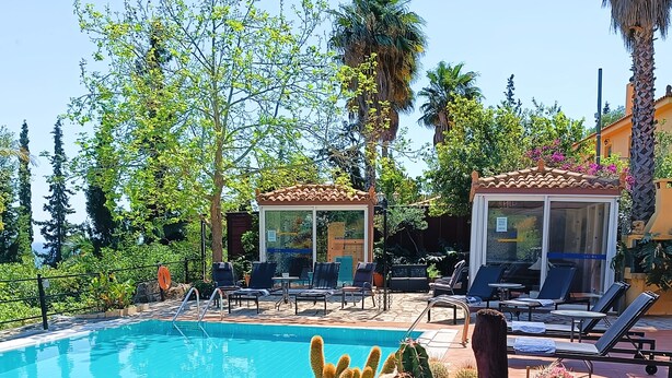 A pool area with lounge chairs, a cactus garden, and a glass-enclosed structure. - Okeanis Apartments & Suites Adults Only (Kefalonia)