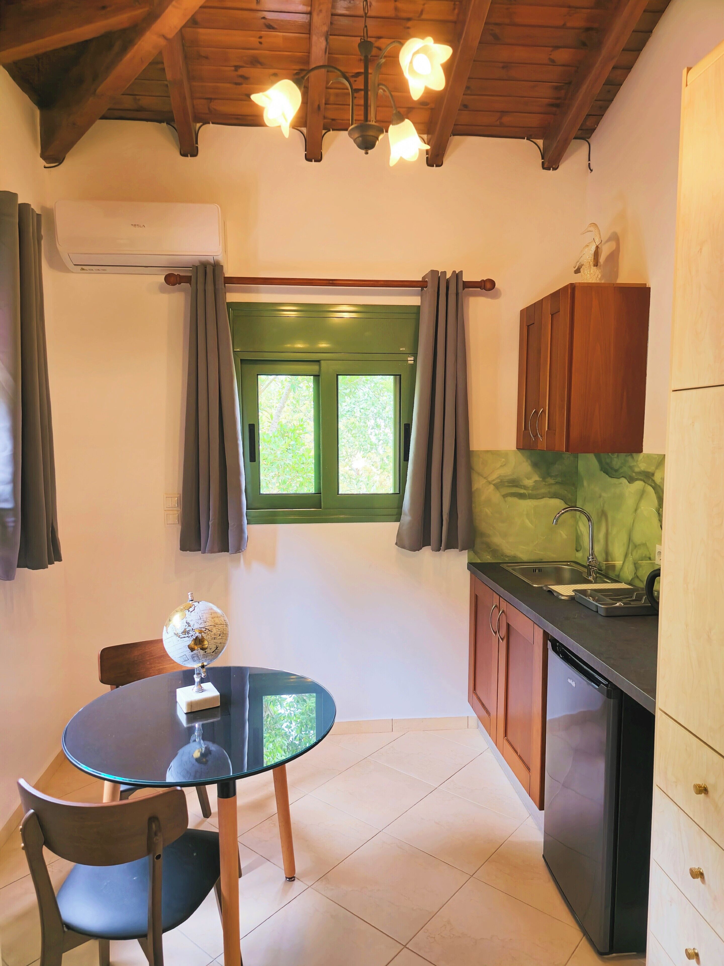 A compact kitchen with a dining area, featuring a round table, chairs, a globe, and a window with curtains.