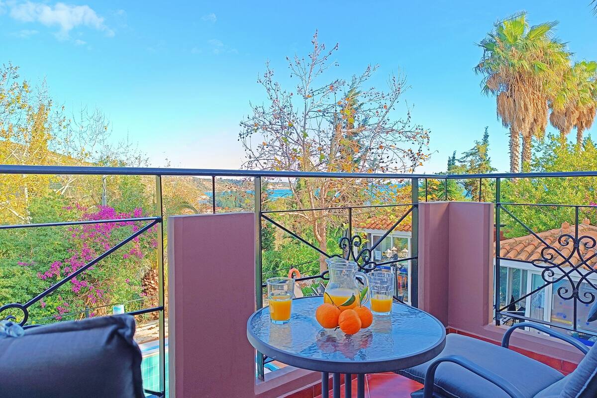 Un balcon avec une table dressée pour deux personnes, agrémenté d’une carafe de jus d’orange et d’oranges fraîches.