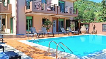 A two-story building with a swimming pool, outdoor seating, and a view of the surrounding greenery.