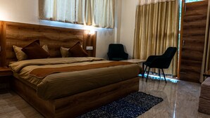 A bedroom with a wooden headboard, a bed with multiple pillows, a nightstand, a desk, two chairs, and a window with curtains. - Winter Stone (Dharamshala)