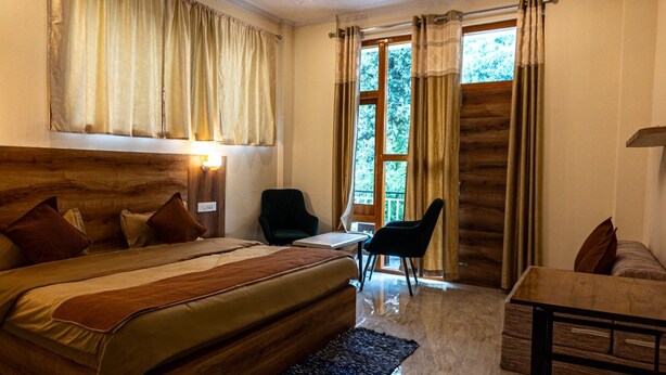 A bedroom with a large bed, two chairs, a small table, and a window with curtains. - Winter Stone (Dharamshala)