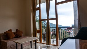 A room with a sofa, a table, and a view of a balcony with a railing and a chair. - Winter Stone (Dharamshala)