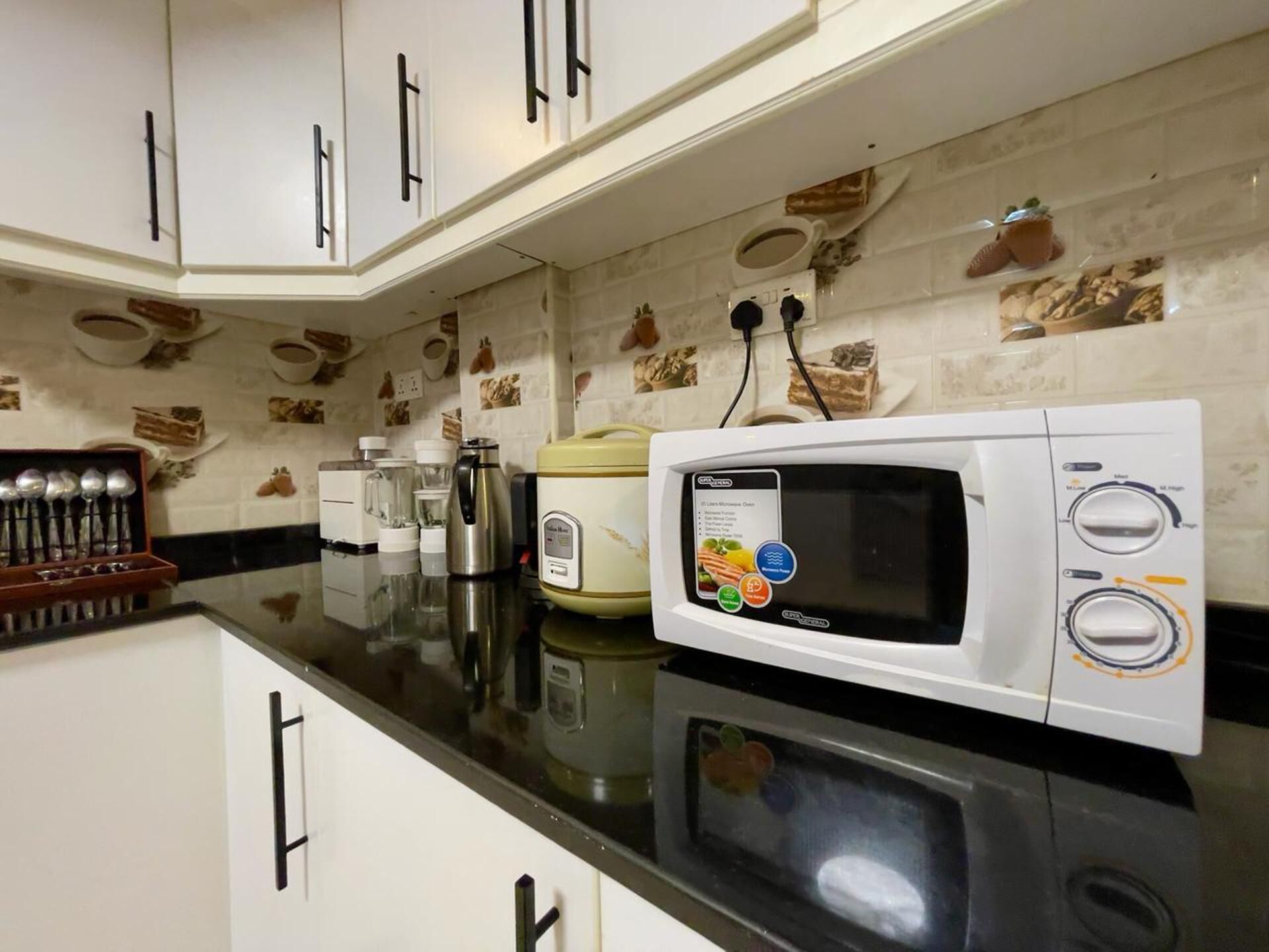 Una cocina con armarios blancos, un microondas, una cafetera y un hervidor sobre la encimera.