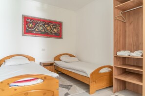 A small, clean room with two wooden beds, a wooden wardrobe, and a decorative wall hanging. - Sunny Valley Guesthouse (Karakol)