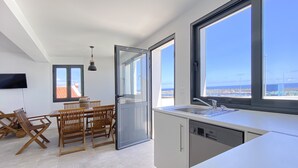 Moderni keittiö, jossa on suuri ikkuna, ruokailutila puisilla huonekaluilla sekä seinälle asennettu taulutelevisio.