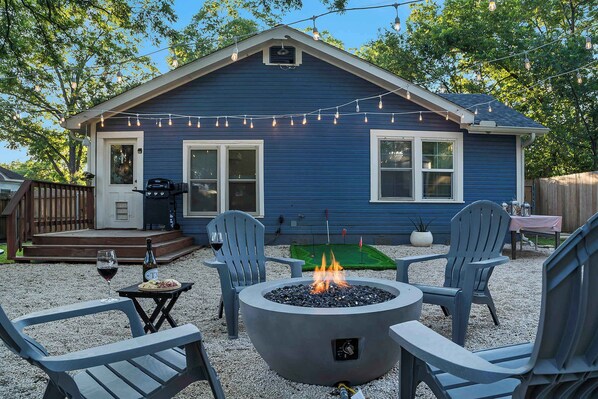 Ein blaues Haus mit Terrasse, Gartenmöbeln, Feuerstelle und Lichterkette.