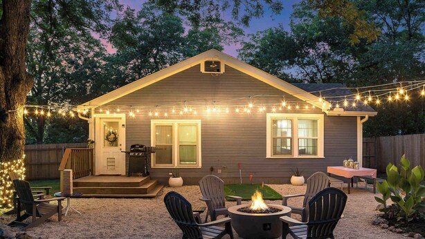 A house with a deck, outdoor seating, a fire pit, and string lights. - Blue Bungalow - Fire Pit, Yard Games & more! (Fredericksburg)
