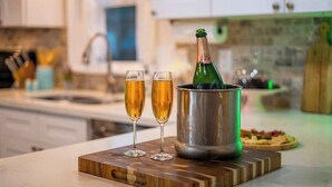 A kitchen with a wooden cutting board, two glasses of champagne, and a bottle in a metal bucket. - Blue Bungalow - Fire Pit, Yard Games & more! (Fredericksburg)