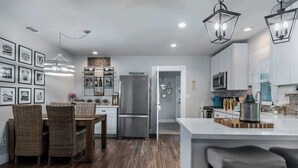 A modern kitchen with a central island, stainless steel appliances, and a dining area with wicker chairs. - Blue Bungalow - Fire Pit, Yard Games & more! (Fredericksburg)